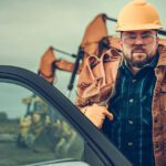 Man getting into a pickup truck on the job site with a yellow hardhat and tool belt