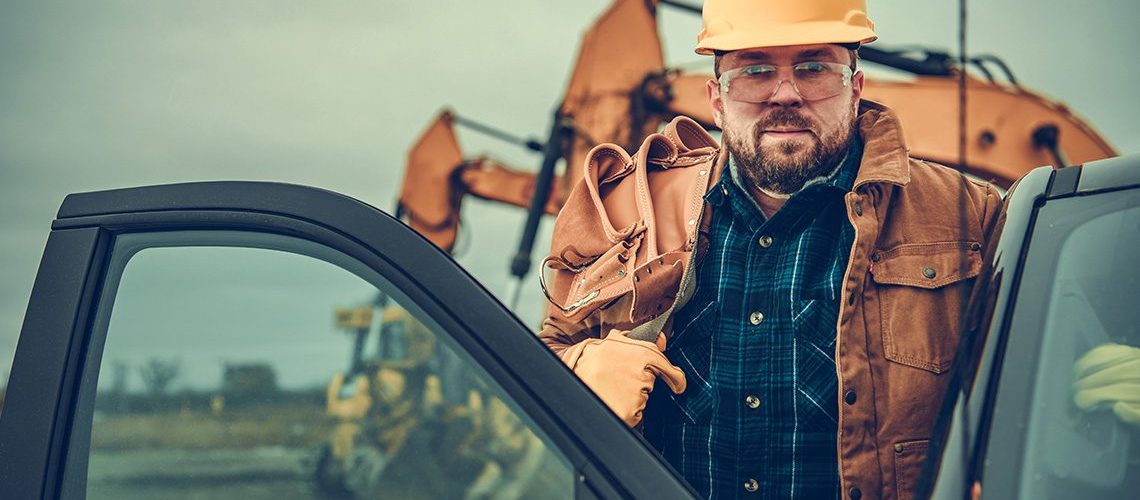 Man getting into a pickup truck on the job site with a yellow hardhat and tool belt